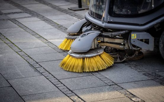 Imagen de una barredora vial en funcionamiento y haciendo su tarea de limpiar las calles